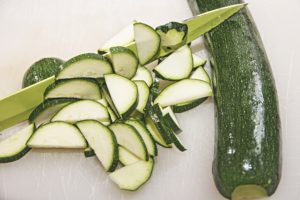 Photo of sliced zucchini, a whole zucchini, and a knife.