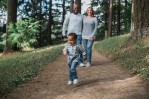 Photo of family (mother, father, and toddler age son) walking on a walking trail together.
