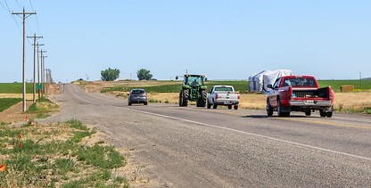 Cars riding behind a tractor on a road.