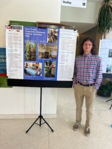 Alexander Kaufhold standing with his internship presentation poster.